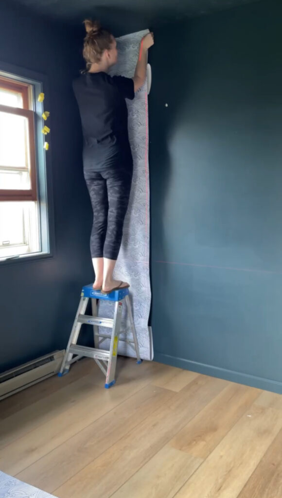 female DIYer hanging wallpaper using a laser level