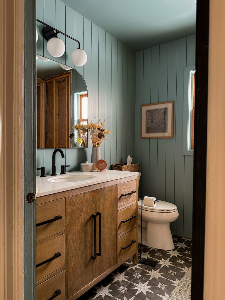 bathroom with blue shiplap walls, black start tile and a wood vanity