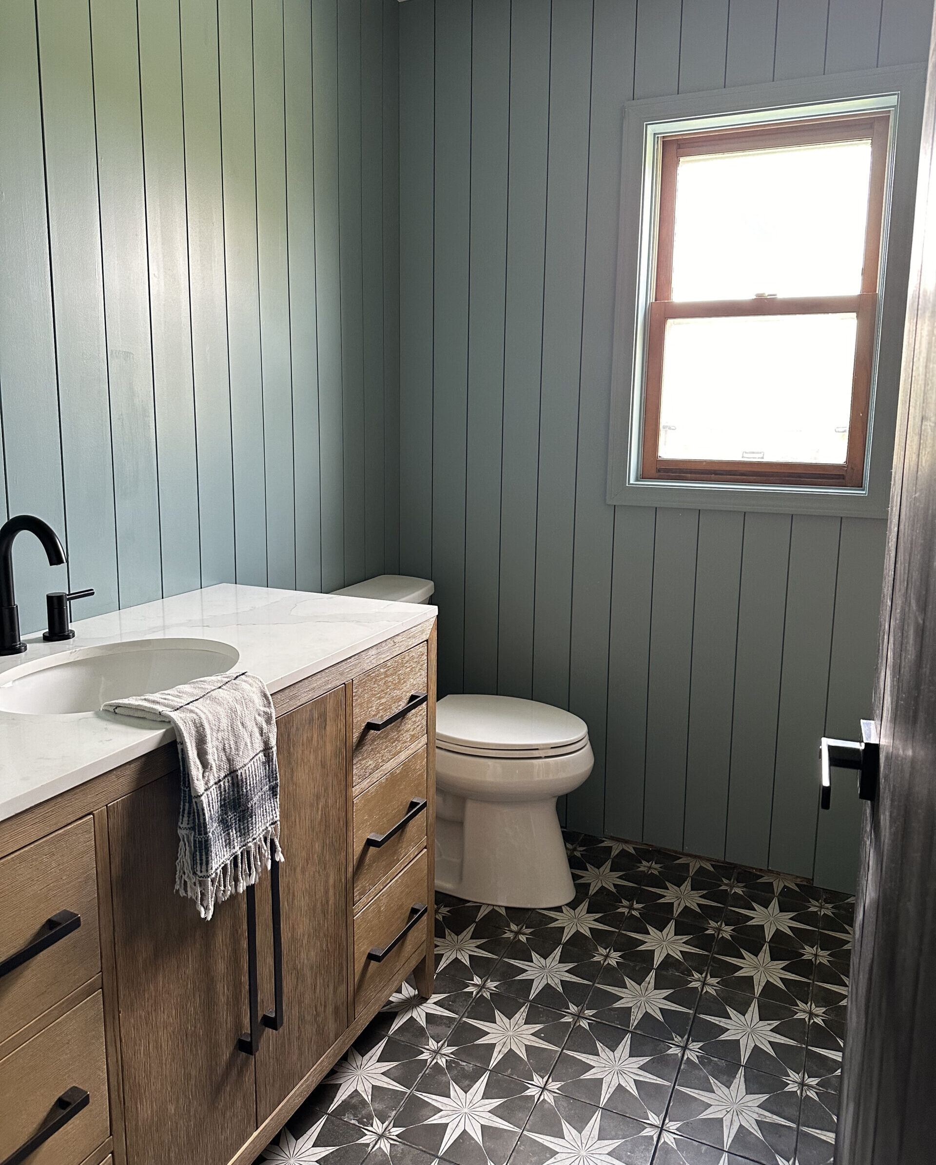 blue vertical shiplap in bathroom with wood vanity and black and white star tile floors